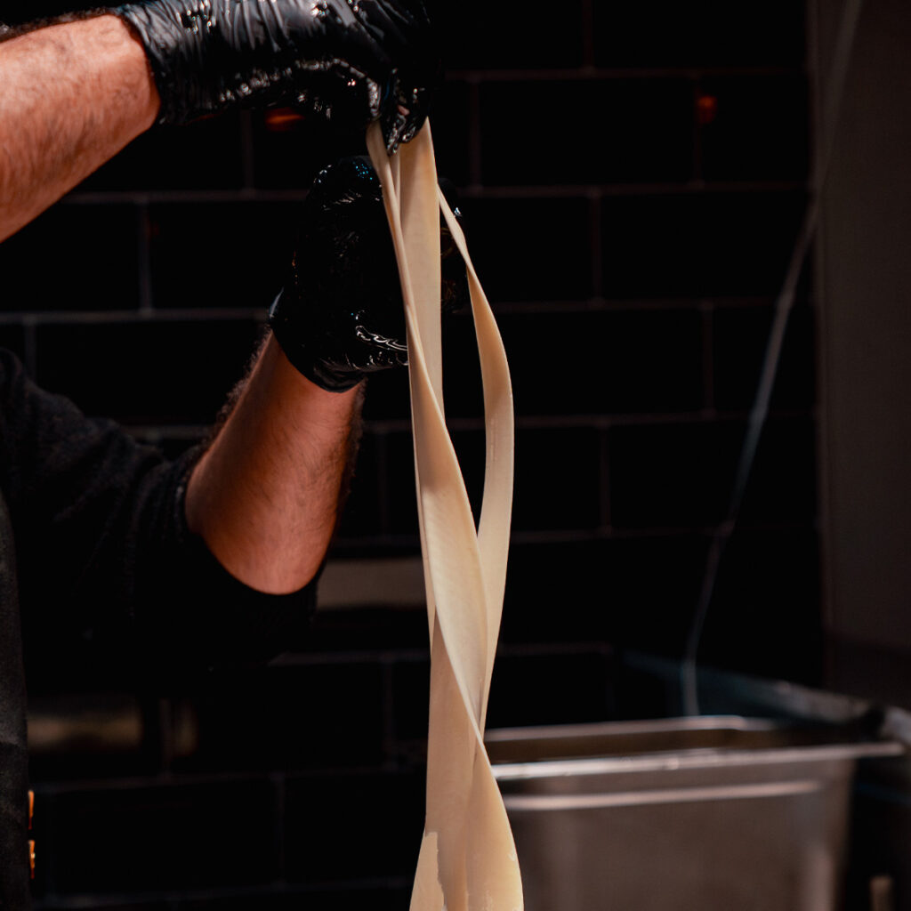 Eine Person formt Teig in einer Küche, trägt schwarze Handschuhe.