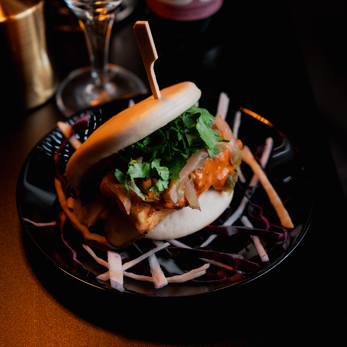 Ein gedämpftes Brötchen mit Gemüse und Sauce, angerichtet auf einem Teller mit dekorativen Streifen.