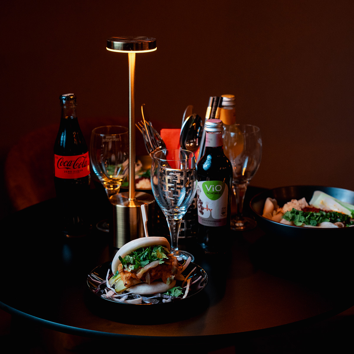 Stimmungsvoll gedeckter Tisch mit gedämpftem Licht, Getränken und asiatischen Gerichten.