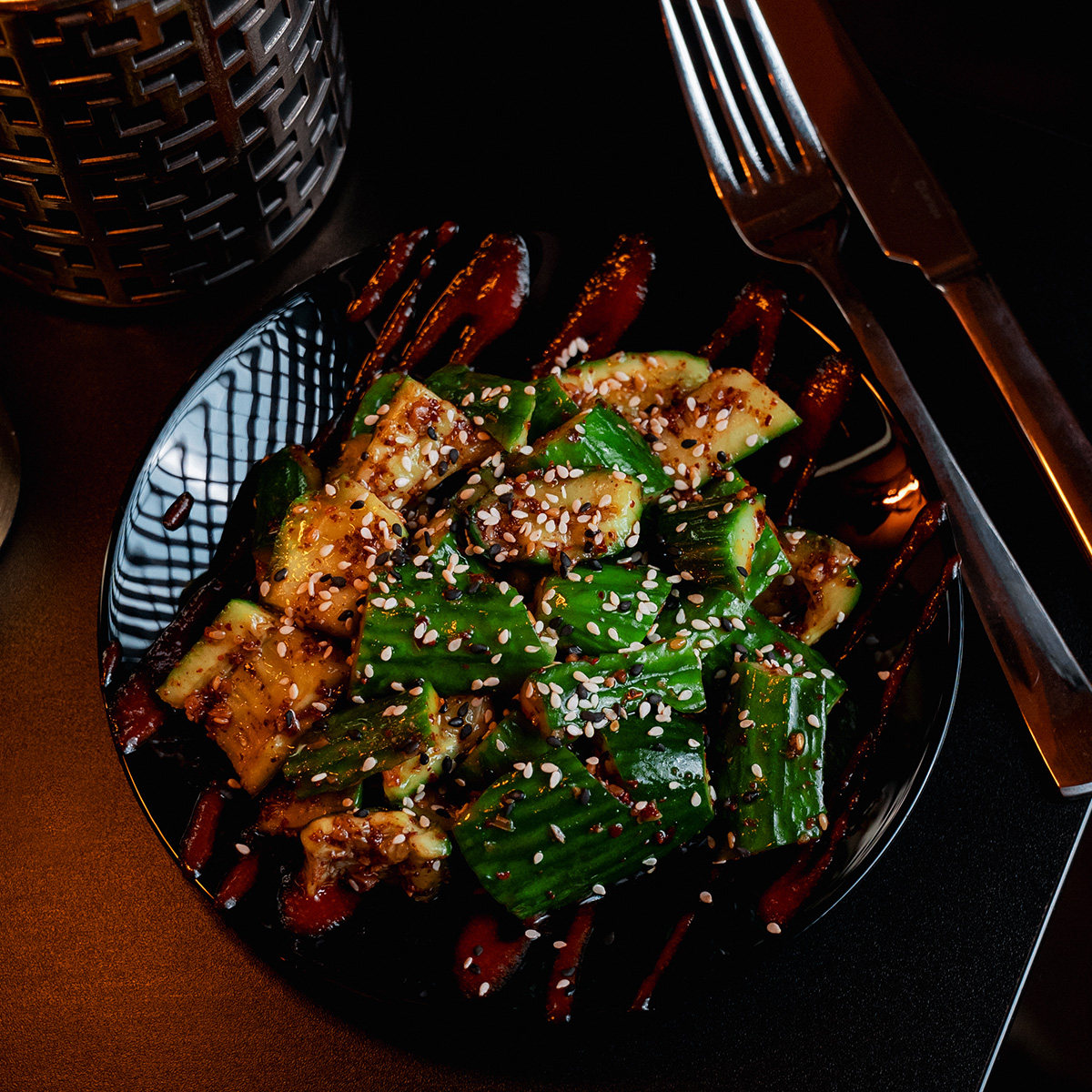 Ein schwarzer Teller mit gewürzten Gurken, Sesam bestreut und kunstvoll angerichtet.