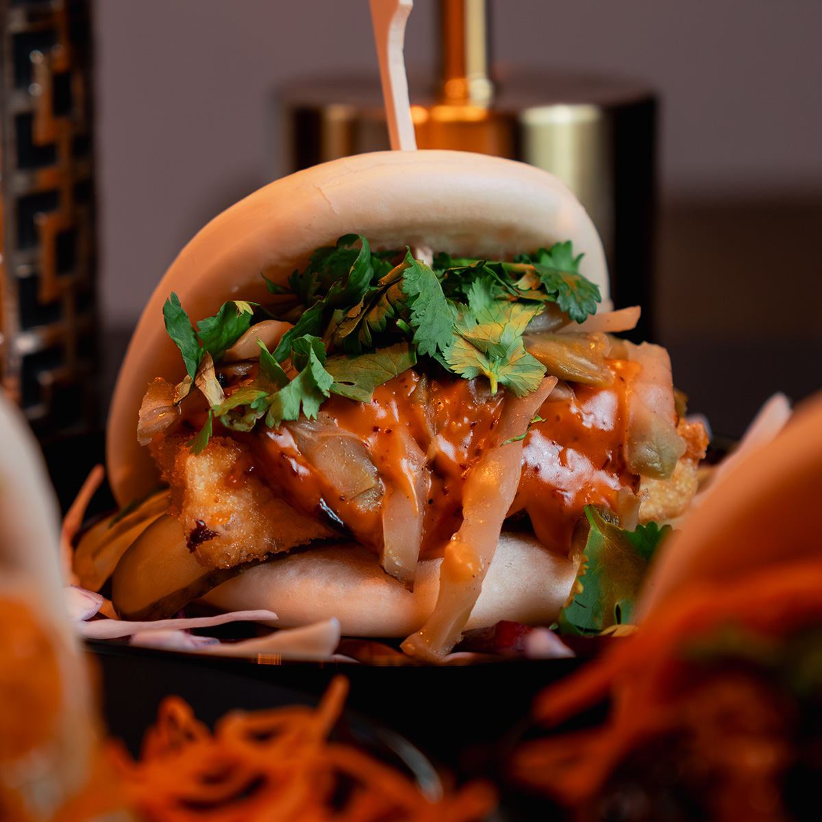 Gedämpftes Brötchen mit knusprigem Tofu, Koriander und Gemüse, serviert auf dunklem Teller.