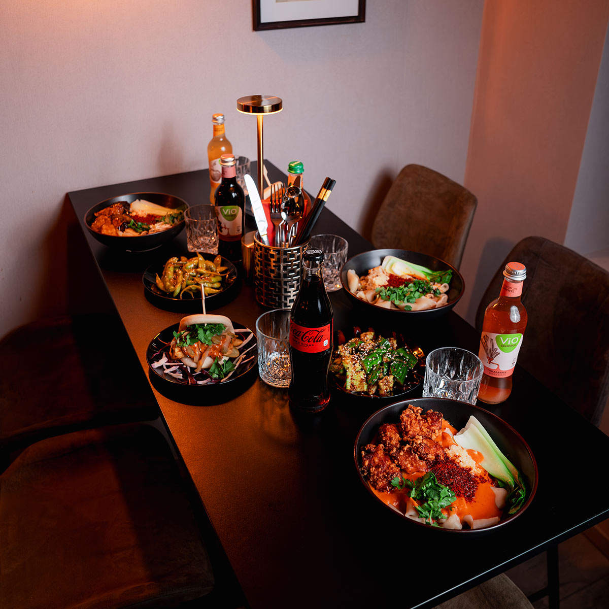 Ein moderner Tisch mit verschiedenen asiatischen Gerichten und Getränken in einer stilvollen Umgebung.